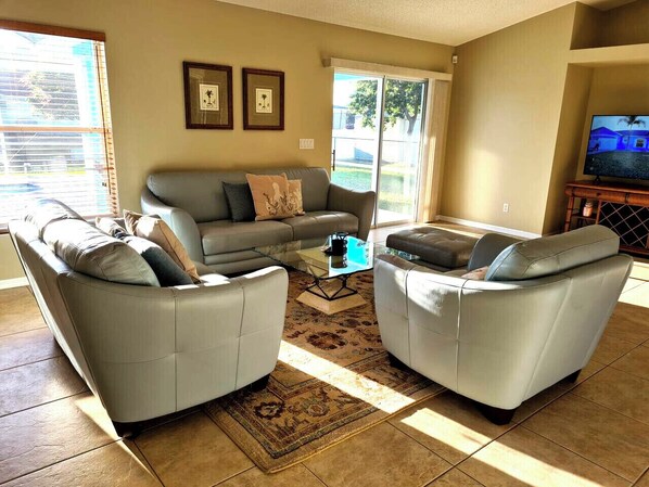 A living room with two grey sofas, a coffee table, and a TV on a wooden stand. - Screened Heated Pool, Boat Ramp Nearby, Beaches (Port St Lucie)