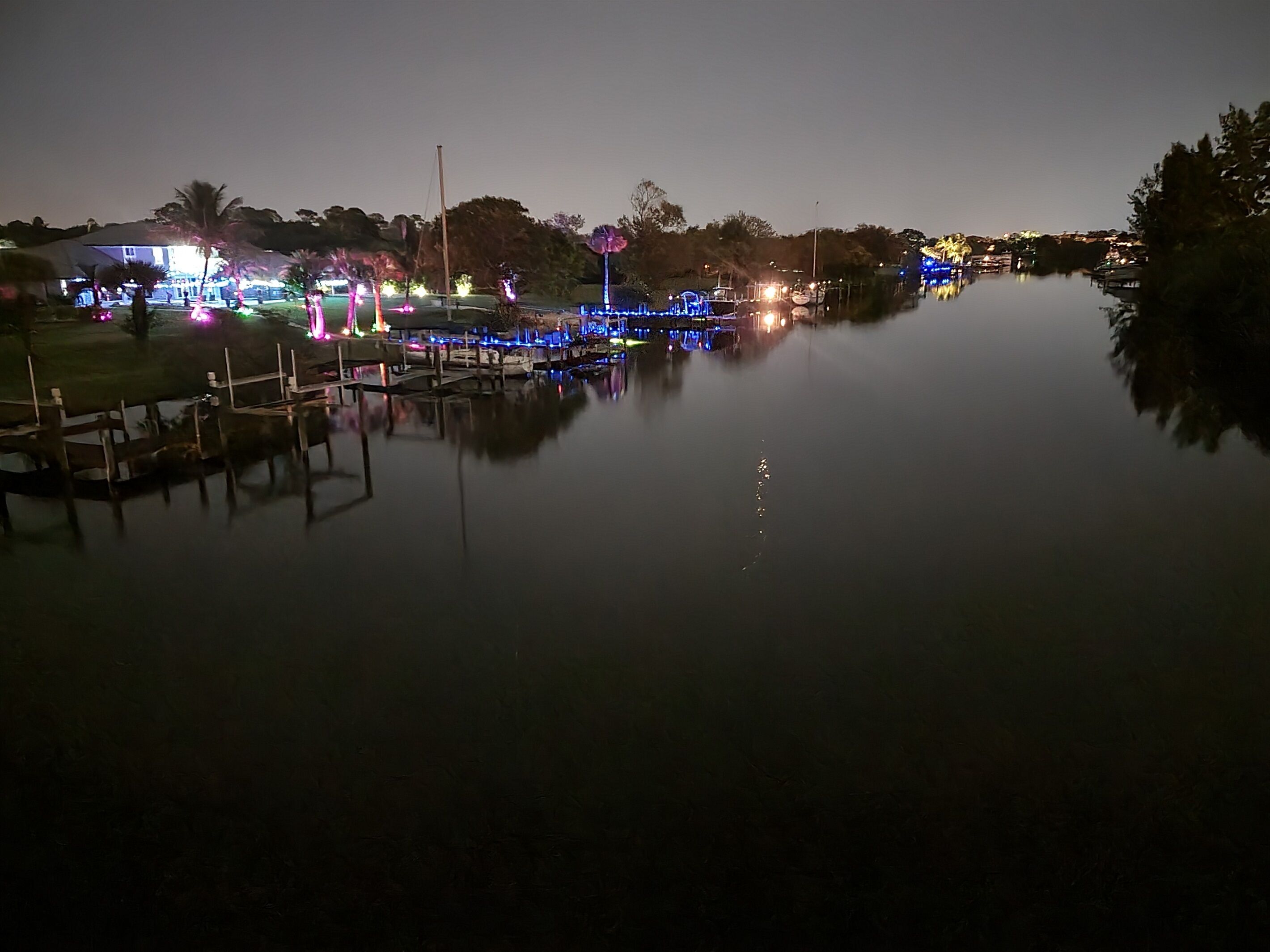 A calm waterfront area with docked boats and a building with colorful lights.