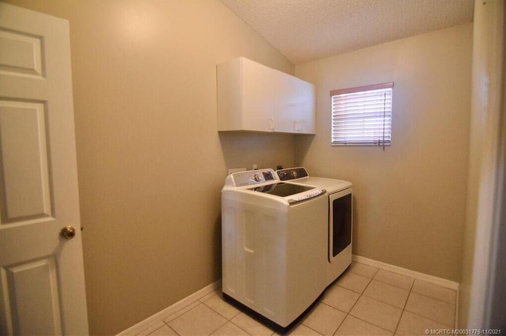 Een wasserette met een wasmachine en droger, een wit kastje en een raam met zonwering.
