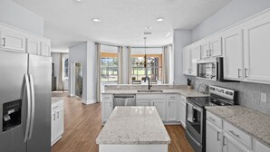 Une cuisine moderne avec des meubles blancs, des comptoirs en granit, des appareils électroménagers en acier inoxydable et un grand îlot central.