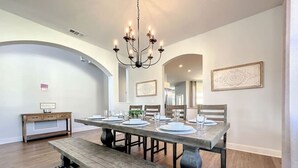 Un coin repas avec une table en bois dressée pour quatre personnes, un banc et un lustre.