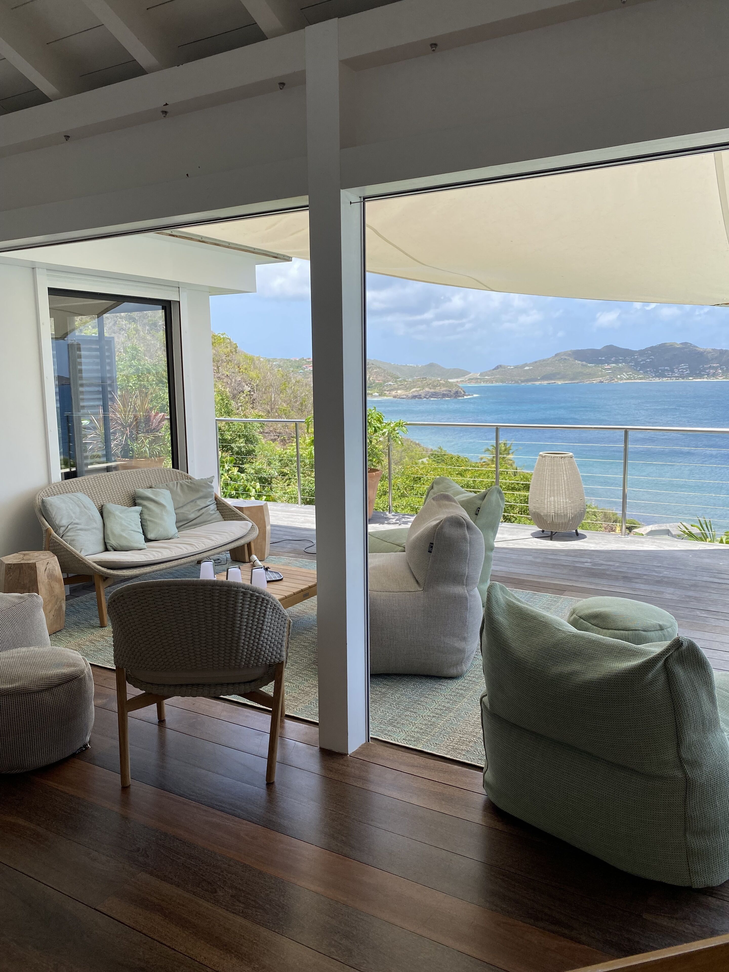 A modern living room with a large sliding glass door leading to a balcony overlooking a scenic ocean view.
