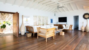A spacious living room with wooden furniture, a stone wall, and a ceiling fan. - Villa Sunset | Ocean View - Located in  Fabulous Pointe Milou with Private Pool (Pointe Milou)