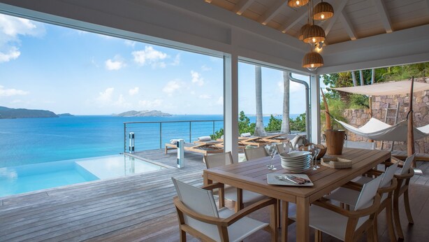 A wooden deck with a glass-bottomed infinity pool overlooking the sea, a dining area with a table set for two, and a hammock with a shade. - Villa Sunset | Ocean View - Located in  Fabulous Pointe Milou with Private Pool (Pointe Milou)