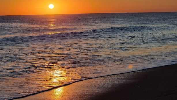 Un coucher de soleil sur une mer calme aux vagues douces.