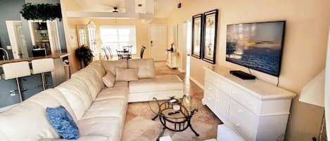 A spacious living room with a large sectional sofa, a glass coffee table, and a flat-screen TV mounted on the wall.
