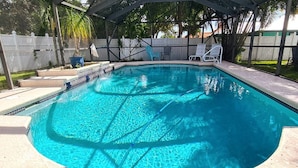 Une piscine rectangulaire dont les bords sont recouverts de carreaux, entourée d’une terrasse couverte aménagée avec des chaises et une table.