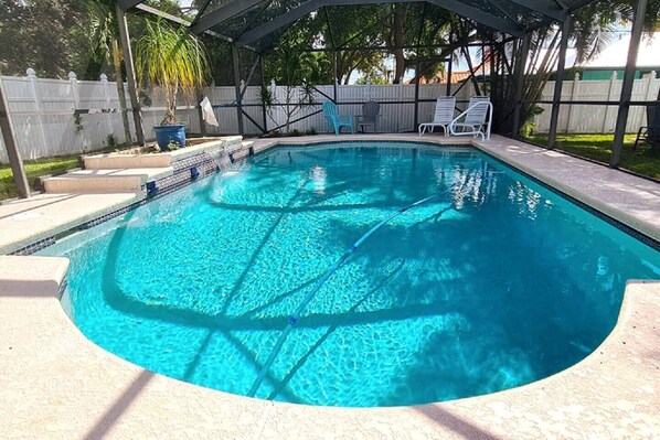 Una piscina rettangolare con bordo piastrellato, circondata da una zona patio coperta con sedie e un tavolo.