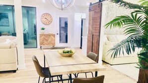 A modern living room with a wooden dining table, two sofas, a large clock, and a sliding barn door. - Huge Deck Overlooking Waller Creek & Lush Backyard (Austin)