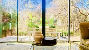 A modern interior with a glass table, a unique sculpture, and a view of a garden through large windows. - Huge Deck Overlooking Waller Creek & Lush Backyard (Austin)