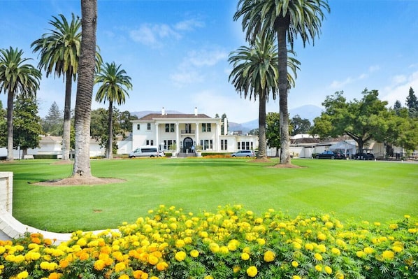A large white building with a symmetrical facade, surrounded by a well-maintained lawn and palm trees.