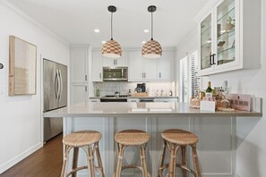 A modern kitchen with white cabinets, a central island with stools, pendant lighting, and a wine rack. - Chic Resort Escape| King Bed + Fireplace + Kitchen (Napa)