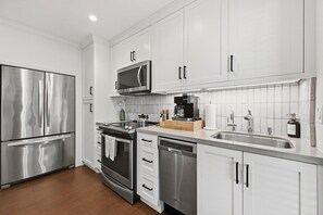 A modern kitchen with stainless steel appliances, white cabinetry, and a tiled backsplash. - Chic Resort Escape| King Bed + Fireplace + Kitchen (Napa)