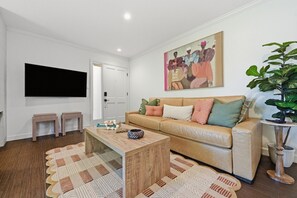 A living room with a beige sofa, a coffee table, two striped side tables, a painting on the wall, and a potted plant. - Chic Resort Escape| King Bed + Fireplace + Kitchen (Napa)