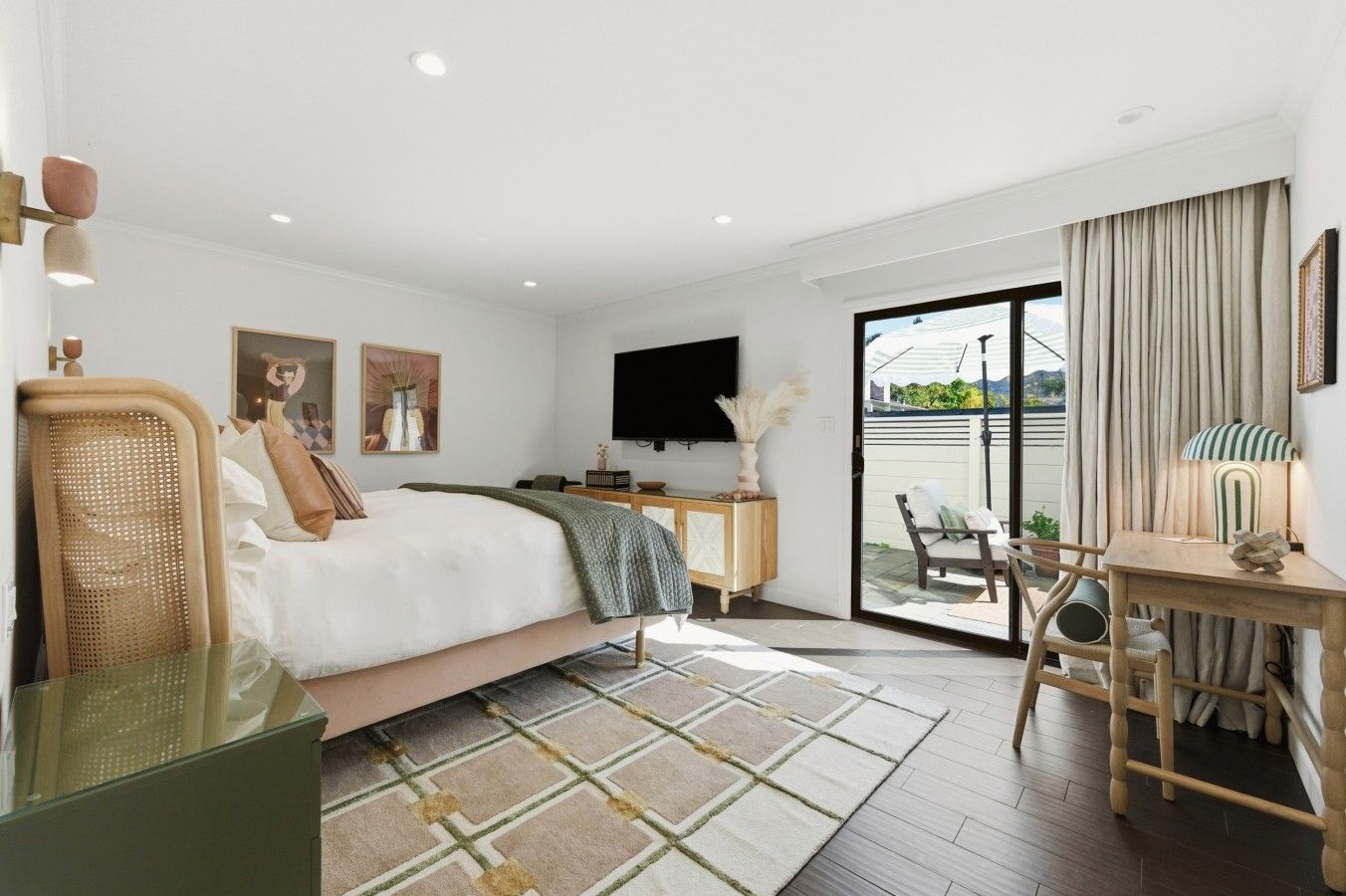 Habitación de hotel con cama, escritorio, silla, televisor y vistas al exterior.