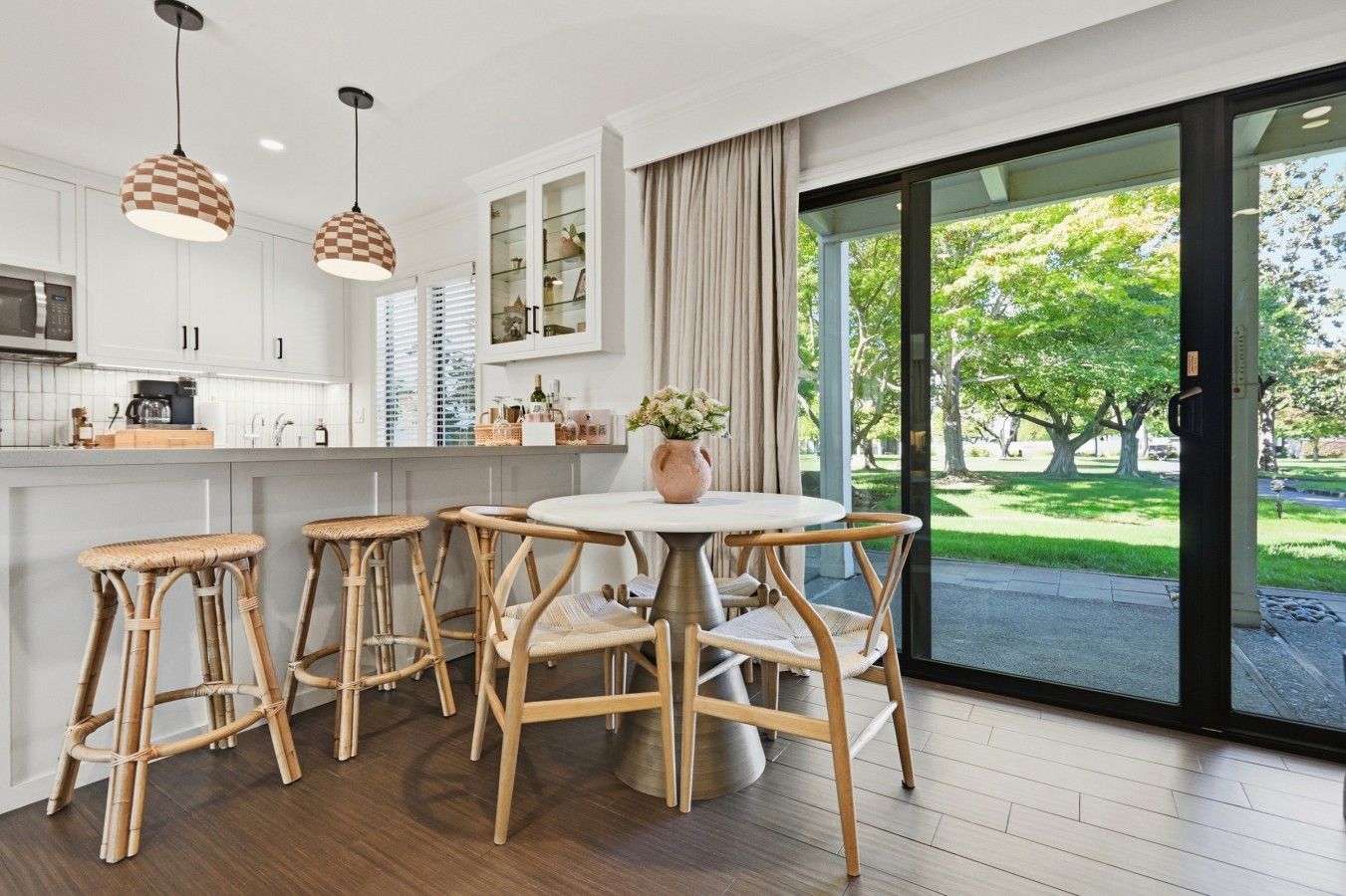 Una cocina moderna con armarios blancos, una mesa de comedor redonda y cuatro taburetes de mimbre.