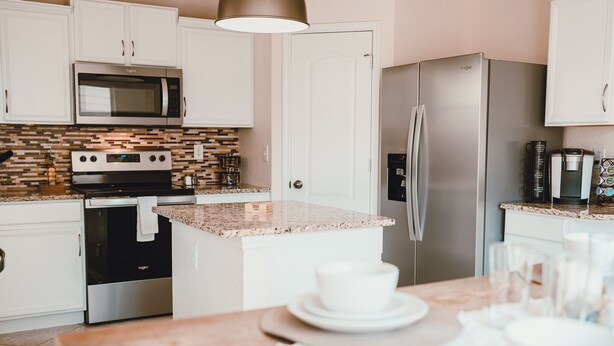 Una cocina moderna con armarios blancos, encimera de granito, electrodomésticos de acero inoxidable y una zona de comedor con mesa para dos.