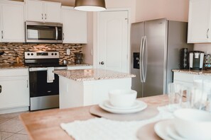 Una cocina moderna con armarios blancos, encimera de granito, electrodomésticos de acero inoxidable y una zona de comedor con mesa para dos.