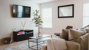 Una sala de estar con televisor de pantalla plana, planta en maceta, mesa de centro, sofá y estantería.