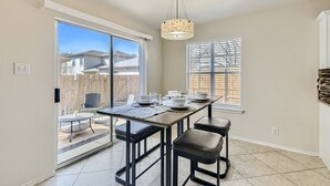 Una cocina con una puerta corrediza de vidrio a un patio, una mesa de comedor con sillas y una lámpara colgante.