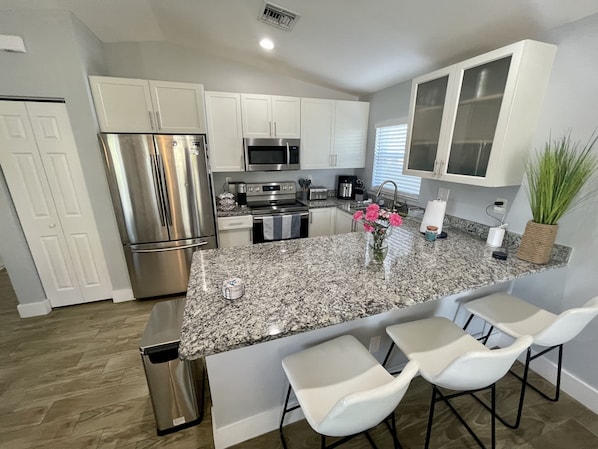 A modern kitchen with granite countertops, stainless steel appliances, white cabinetry, and a small island with bar stools.