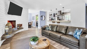 Een moderne woonkamer met een open haard, een wandgemonteerde televisie, een leren bank en een eethoek op de achtergrond.