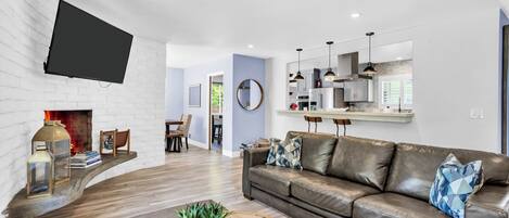 Un salon moderne avec une cheminée, un téléviseur fixé au mur, un canapé en cuir et un coin repas à l’arrière-plan.