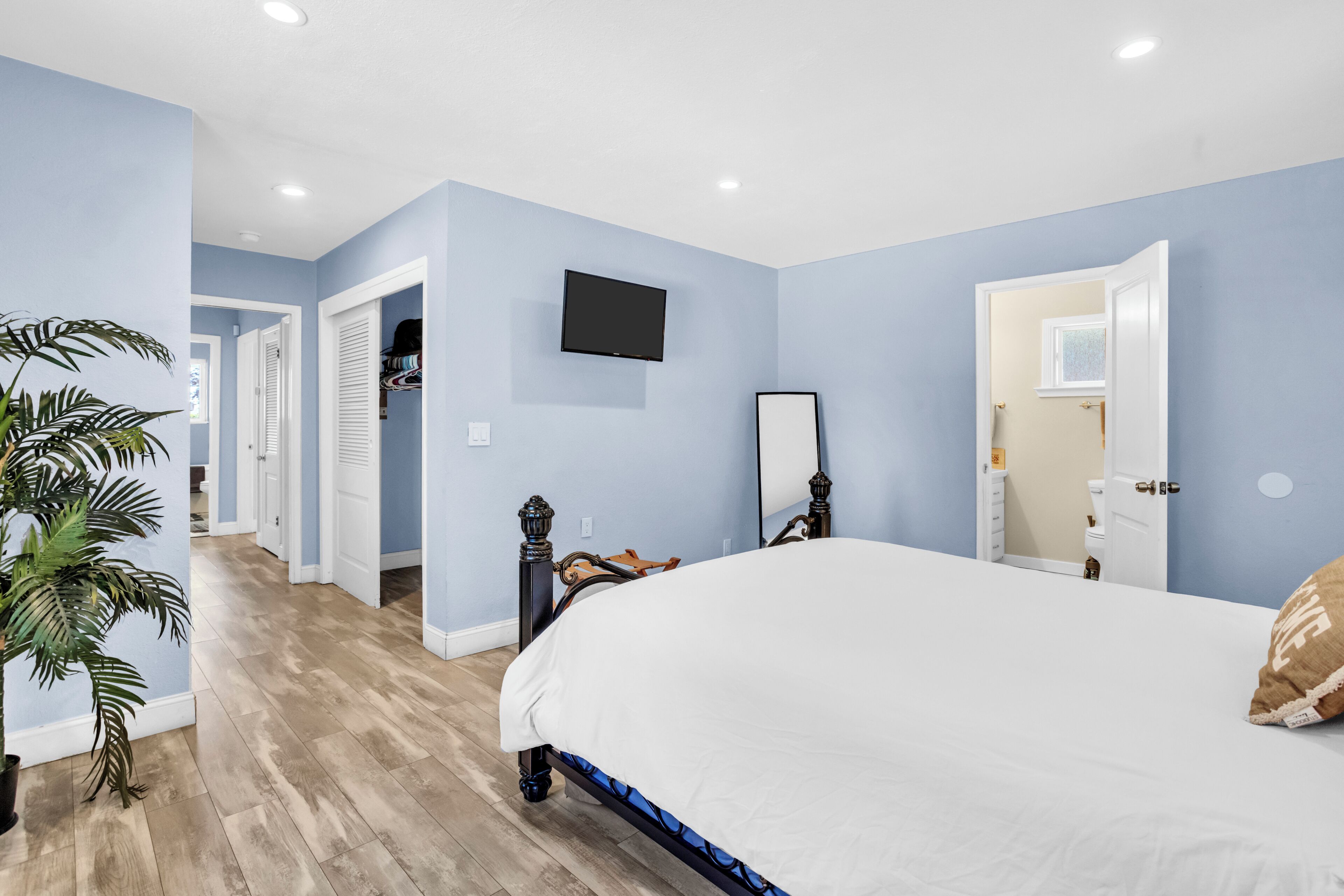 A bedroom with a bed, a television, a mirror, and a door leading to another room.