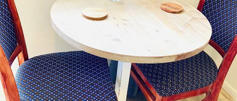 Uma mesa redonda de madeira com um vaso de flores, rodeada por quatro cadeiras com estofados estampados em azul.