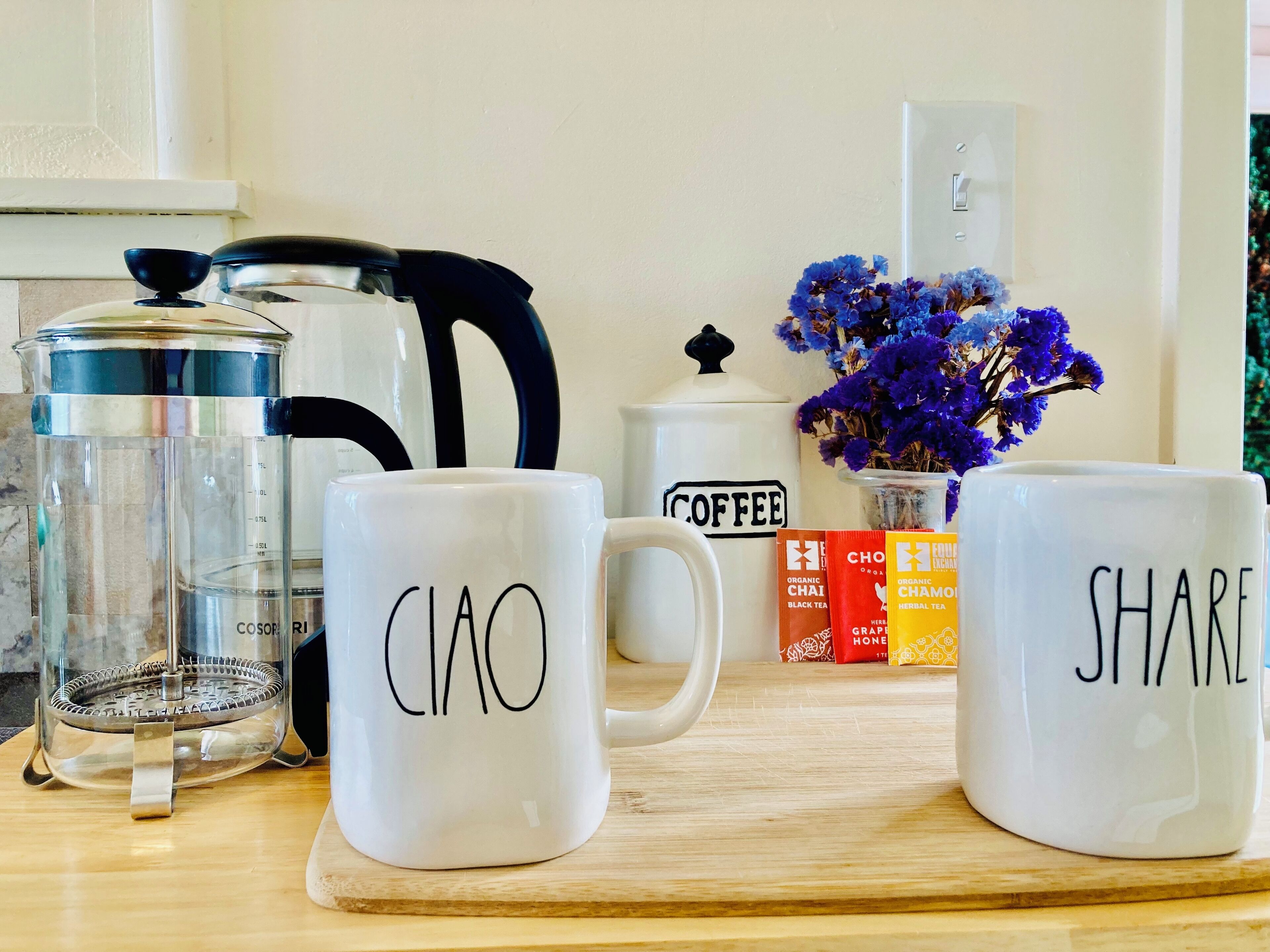 A kitchen counter with a coffee maker, a kettle, and two mugs with "CIAO" and "SHARE" written on them.