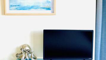 A room with a TV on a light blue dresser, a framed painting above it, and a curtain to the right.