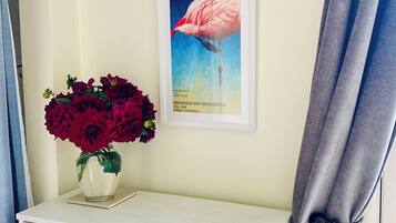 A white cabinet with a patterned tile design, a framed artwork of a flamingo, and a vase of red flowers on top.