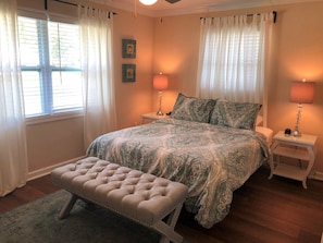 A bedroom with a large bed, two bedside tables with lamps, a bench, and curtains.
