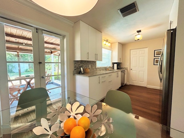 A kitchen with white cabinets, a countertop, and a refrigerator. There is a dining table with chairs and a glass top.