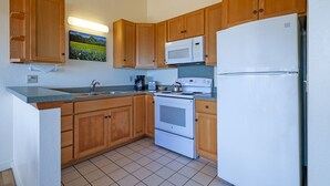 A kitchen with wooden cabinets, a white refrigerator, a microwave, a stove, and a sink. - Full 🌊 Views & 🌋Views Watch the🌅 and 🌕 rise (Koloa)
