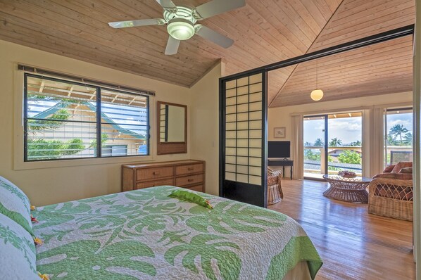A bedroom with a bed, dresser, and sliding glass door leading to a balcony with wicker furniture.