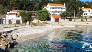 Una propiedad costera con una playa despejada, un edificio blanco de techo rojo y un litoral rocoso.