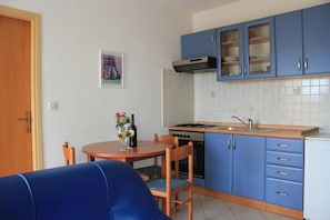 A compact kitchen with blue cabinets, a stove, and a dining area with a table and chairs.