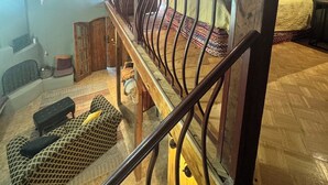 Ein geräumiger Loft mit hoher Decke, freiliegenden Holzbalken, einem Balkon mit schmiedeeisernem Geländer und einem großen Fenster, das für natürliches Licht sorgt.