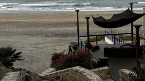 Blick auf einen Strand von einer überdachten Terrasse mit Steinmauern und einem Holzgeländer.