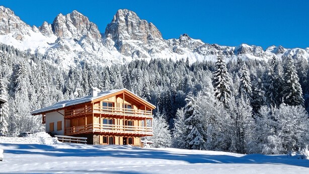 Een houten chalet met een balkon, omringd door sneeuwbedekte bomen en bergen.