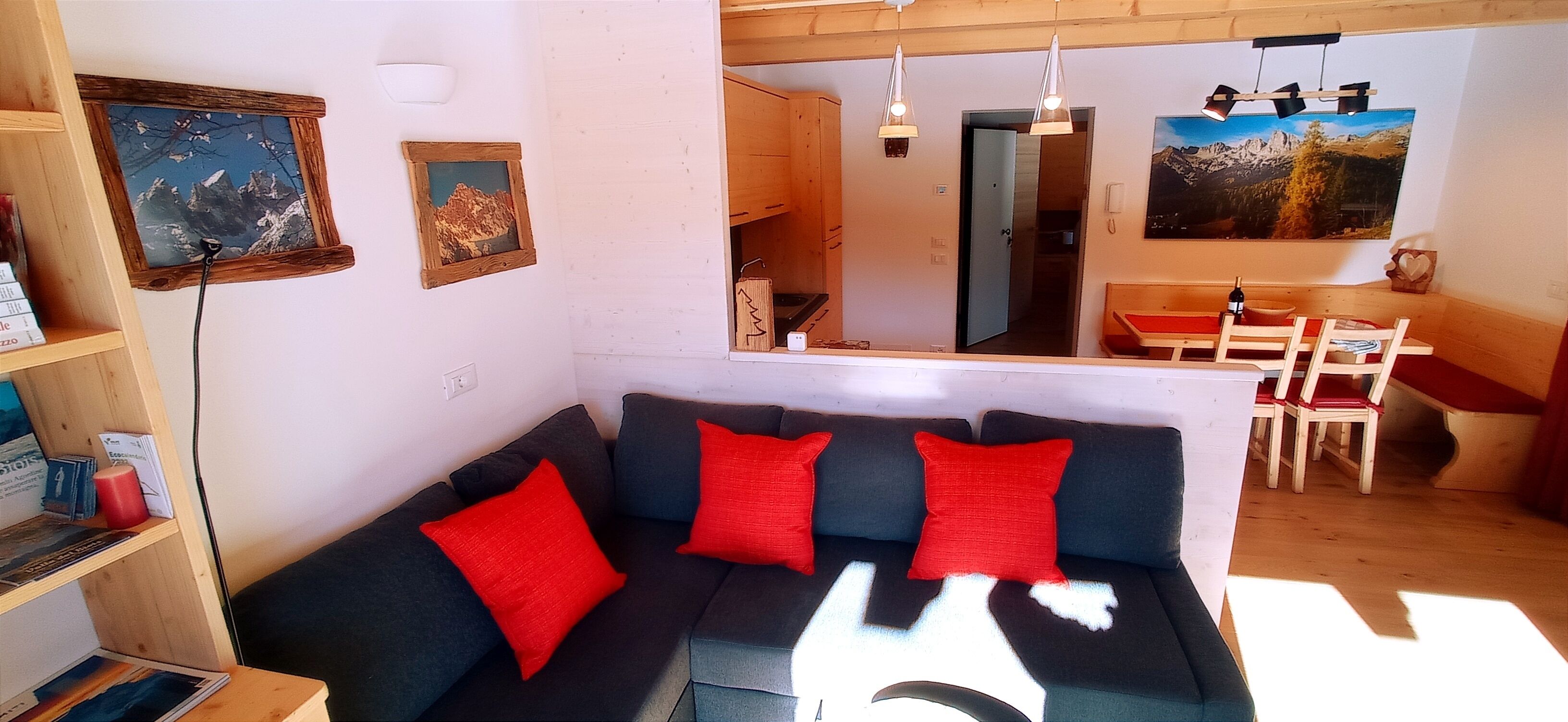 Uma sala de estar aconchegante com um sofá preto, almofadas vermelhas e uma estante de madeira.