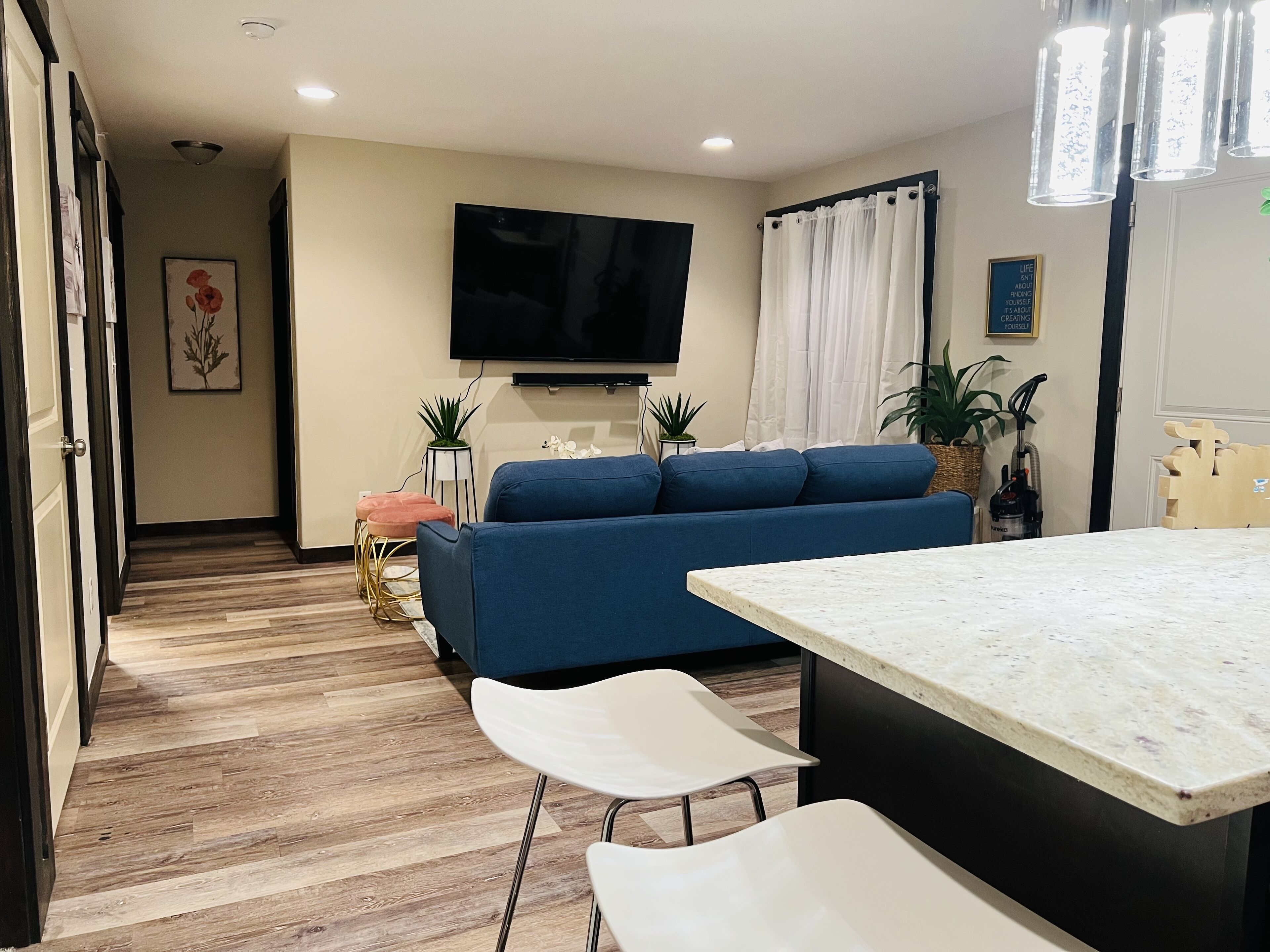 A modern living room with a blue sofa, a flat-screen TV, a dining table with chairs, and a kitchen area with a countertop.