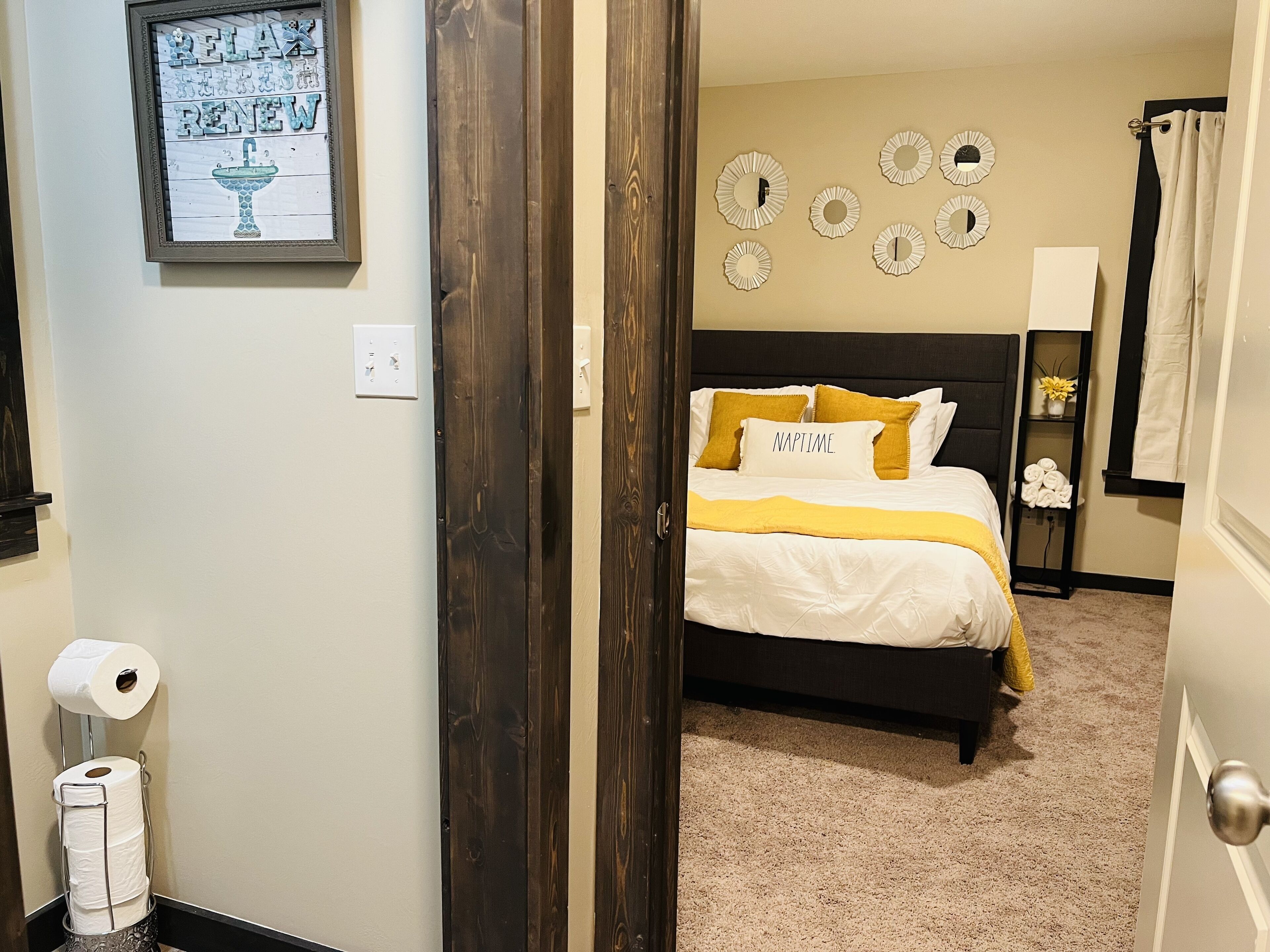 A bedroom with a bed, a wall-mounted mirror, a framed picture, and a toilet paper holder.