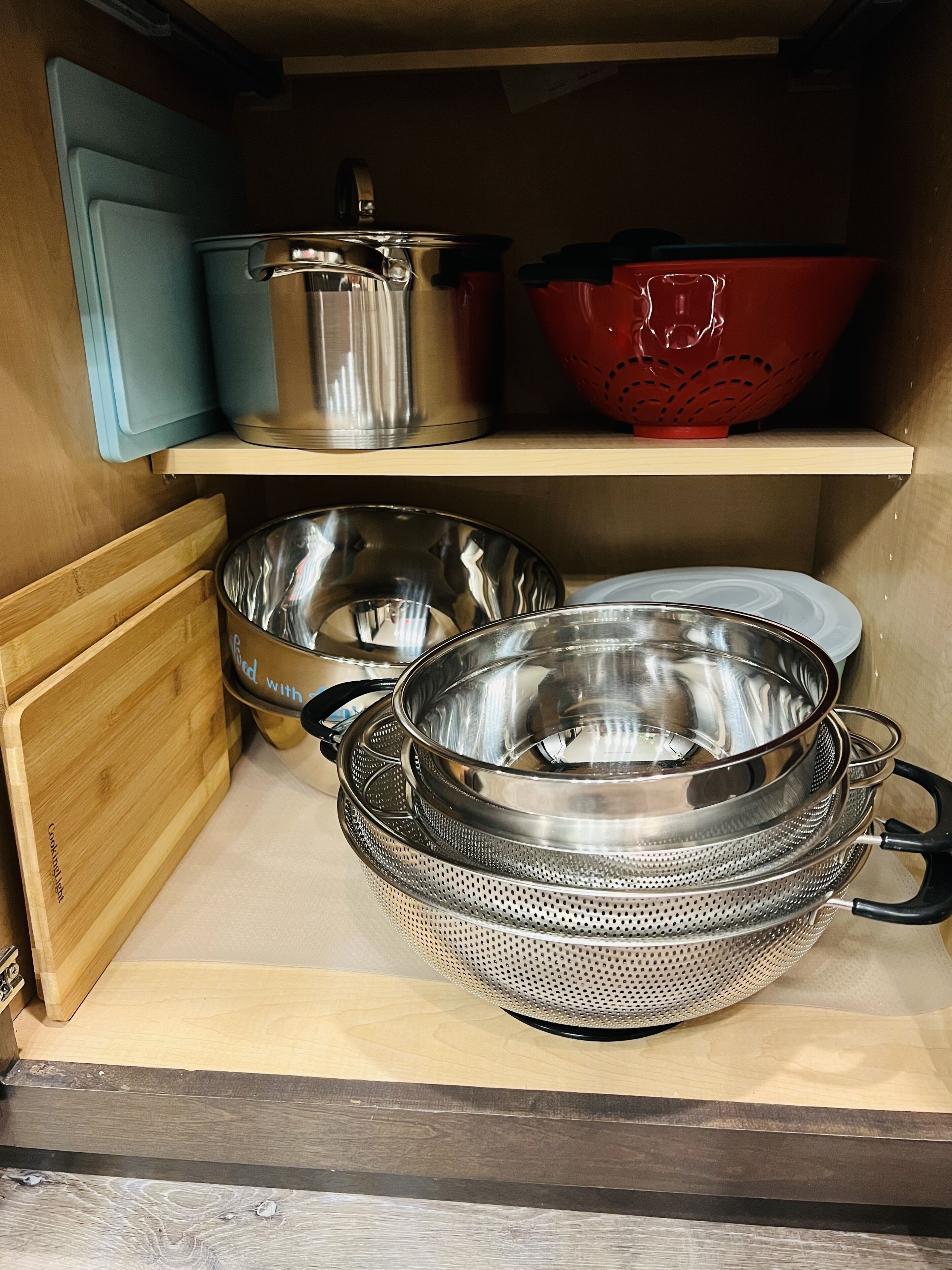 Una cocina con utensilios de acero inoxidable, un colador rojo y una tabla de cortar de madera.