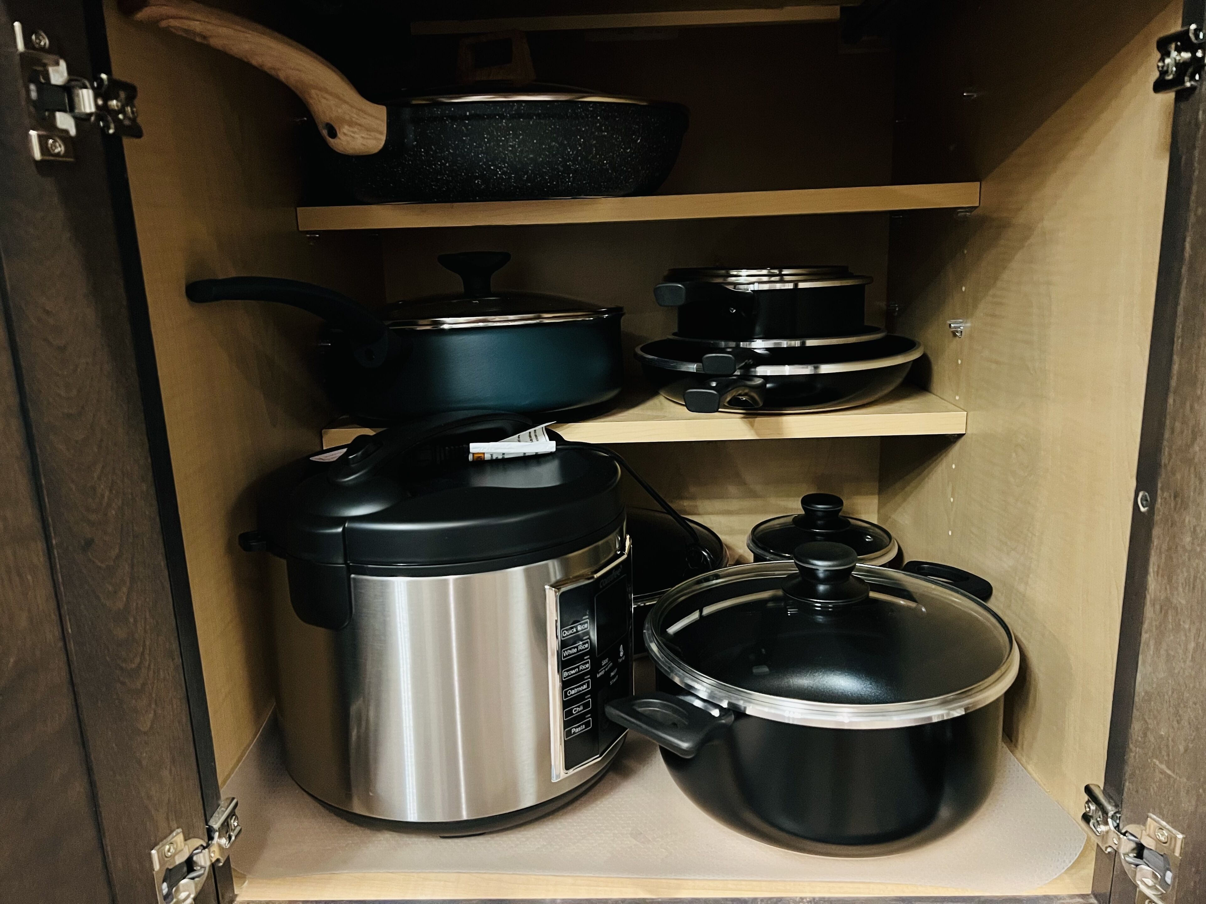 A kitchen cabinet with various cooking pots and a rice cooker.