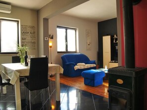 A living room with a dining table, blue sofa, and a black stove.