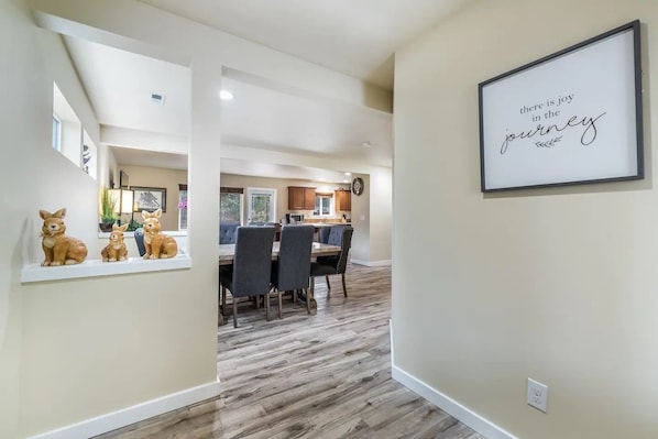 A hallway leading to a dining area with a kitchen in the background, a framed inspirational quote on the wall, and a shelf with rabbit figurines. - Perfect Private Getaway Minutes to Downtown! (Tacoma)