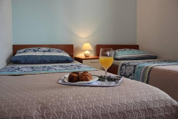 A hotel room with a bed, two pillows, a bedside table with a lamp, and a tray with croissants and a glass of orange juice.