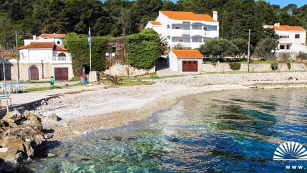 Una proprietà costiera con spiaggia limpida, un edificio bianco con tetto rosso e un litorale roccioso.